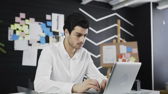 Businessman Looks at the Camera Then Starts Working on Notebook