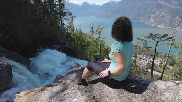 Adventurous Adult Woman is Sitting on Top of a Beautiful Waterfall