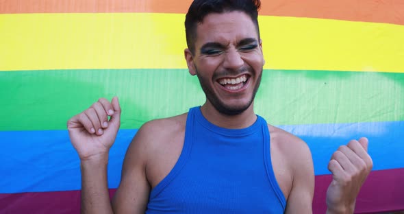 Young transgender man with make up dancing in front of rainbow flag