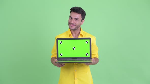 Happy Young Hispanic Businessman Thinking While Showing Laptop