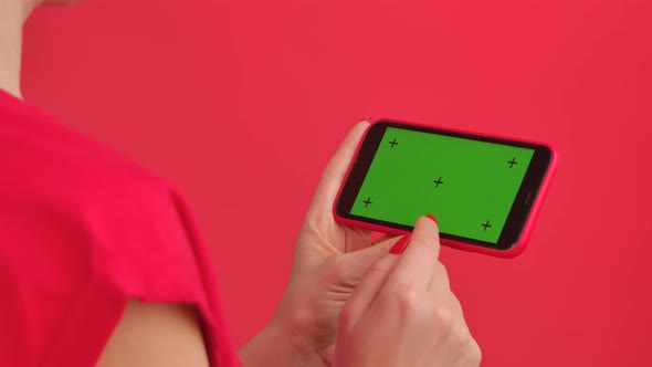 Woman Holds Mobile Phone with Green Workspace Mock Up Screen in Her Hands on Red Studio Background