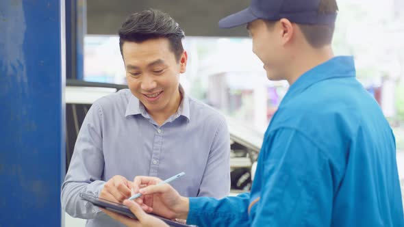 Asian automotive mechanic explain car condition to client in garage.