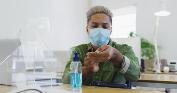 Man wearing face mask sanitizing his hands at office