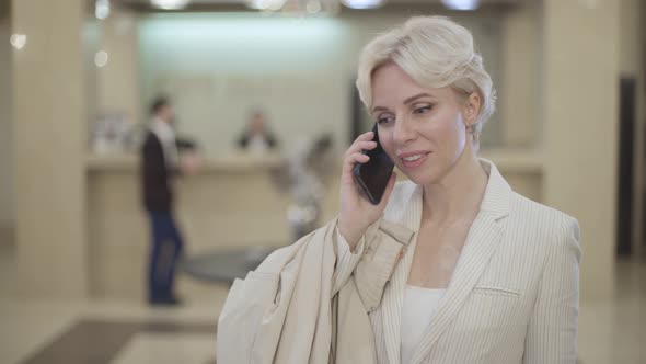 Portrait of Cheerful Caucasian Blond Woman Hanging Up and Looking at Camera