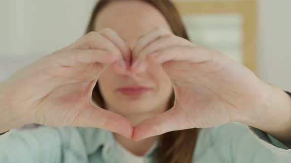 Young Woman Smiles and Makes a Heart Shape with Her Fingers