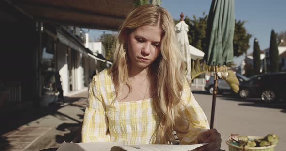 Beautiful Blonde Woman Sitting Outside Reading a Magazine on a Sunny Day