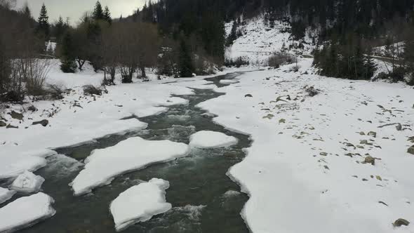 Aerial View in Winter on a Mountain River with a Forest During a Snowfall