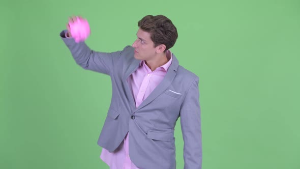 Stressed Young Businessman Holding Piggy Bank and Giving Thumbs Down