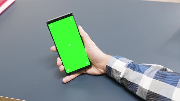 Man Holding a Green Screen Phone on the Table