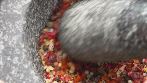 Closeup of a Pestle Grinding and Mixing Various Spices Peppers and Sea Salt