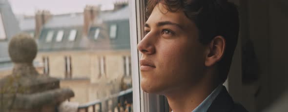 Attractive young european man looking out of the window, looking up and smiling