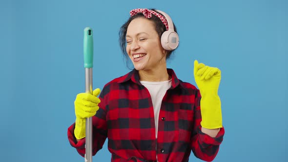 Emotional Young Woman Wearing Headphones Singing Into Mopand Dancing Laughing Over Blue Background