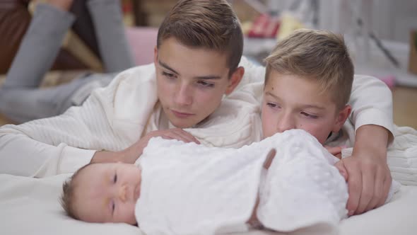 Teenage Brothers Admiring Infant Baby Sister Stroking Child Head in Slow Motion