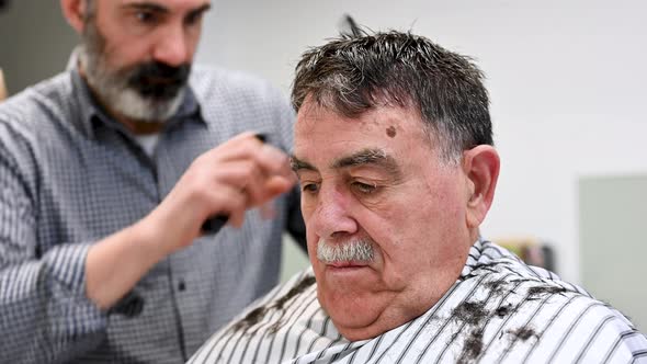 Barber Trimming Hair of Old Man at Barber Shop.