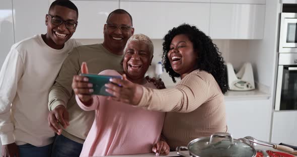 Happy latin family cooking inside kitchen at home and taking a selfie with mobile phone