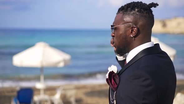 Side View of Busy African American Groom in Suit Talking on the Phone with Picturesque Turquoise