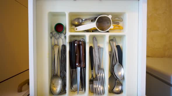 Top down view of hands opening kitchen cutlery draw, removing knife and fork then closing draw.