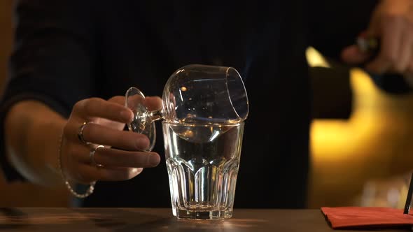 The bartender sets fire to the sambuca in a beautiful wine glass and pours it into another