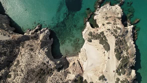 White rocky cliffside towers over crystal-clear turquoise blue Mediterranean waters. Summertime Milo