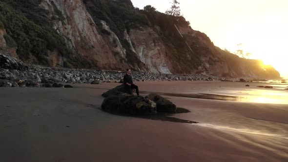 A man sitting in peaceful meditation and mindfulness on the calming sandy beach with ocean waves at