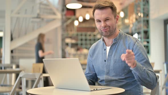 Casual Man with Laptop Pointing at Camera in Cafe 