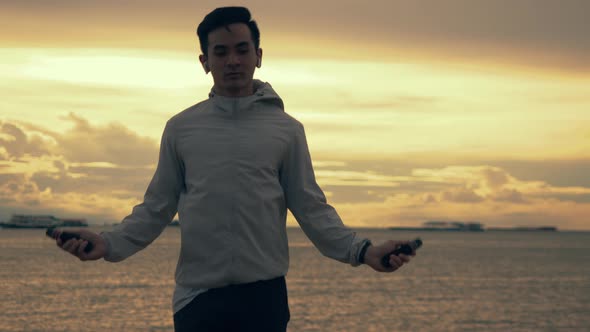 Asian sportsman in sports clothing skipping rope while exercising workout on the beach.