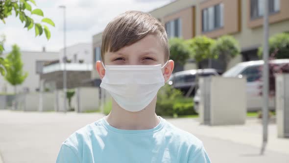 A Young Boy in a Face Mask Looks at the Camera in an Empty Suburban Area