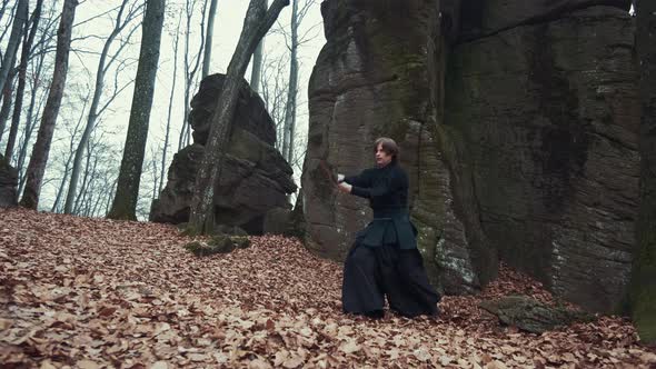 Man in Traditional Japanese Clothes, with a Sword, a Katana, Trains Martial Arts in the Forest