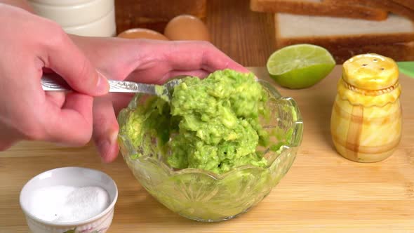 Hands mashing avocado with fork in a bowl, male chef hands preparing guacamole recipe. Cooking