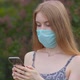 A young girl in a protective medical mask looks at the phone and sends messages - VideoHive Item for Sale