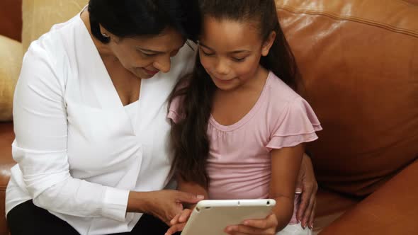 Grandmother and granddaughter using digital tablet in living room 4k