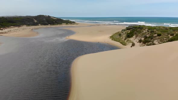 A moving forward aerial shot of a beautiful river mouth and estuary behind the sand dunes on the coa