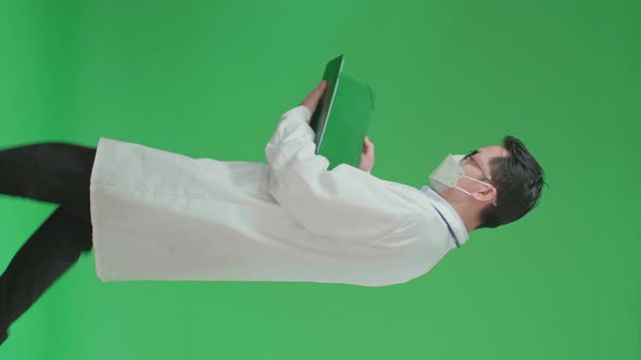 Asian Doctor With Stethoscope Wearing Mask, Opening Document File While Walking On Green Screen