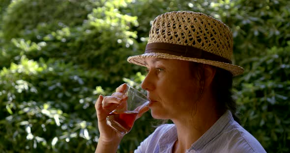 Relaxed Tourist Woman with Straw Hat Is Sipping Hot Tea in Garden Cafe in Summer Day