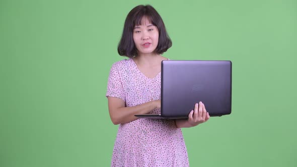 Happy Asian Pregnant Woman Talking While Using Laptop