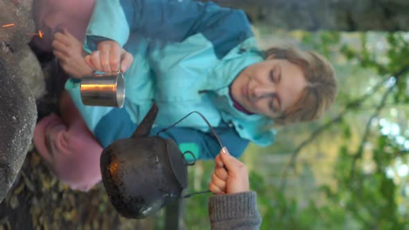 Two Female Friends Make Coffee in a Kettle on an Open Fire in the Forest, A Vertical Video