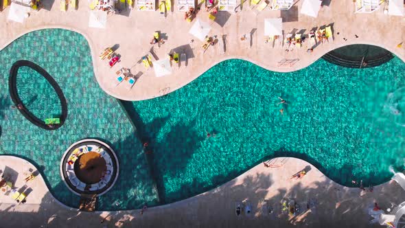 Fly Over a Large Pool with Blue Water and a Lot of Tourists in Hot Weather