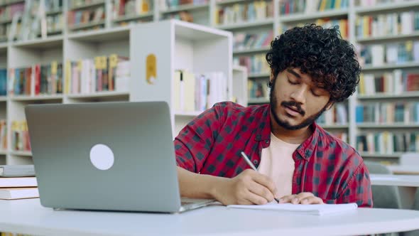 Focused Clever Arabian or Indian College Student Sits at Table with Laptop in University Library