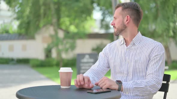 Middle Aged Man Looking Smartwatch While Waiting in Outdoor Cafe