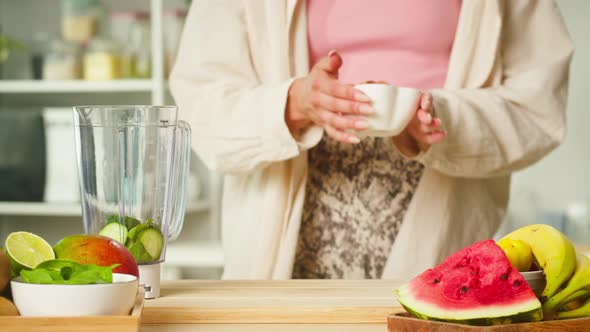 Woman Putting Almonds Into Blender with Cucumber Closeup Cooking Green Detox Smoothie in the Kitchen