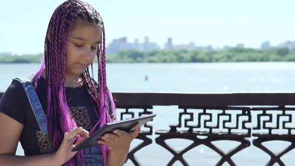 Young Girl Uses a Tablet Standing By the River