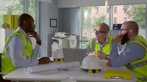 Multiethnic Team of Construction Workers Sitting in Office and Collaborating