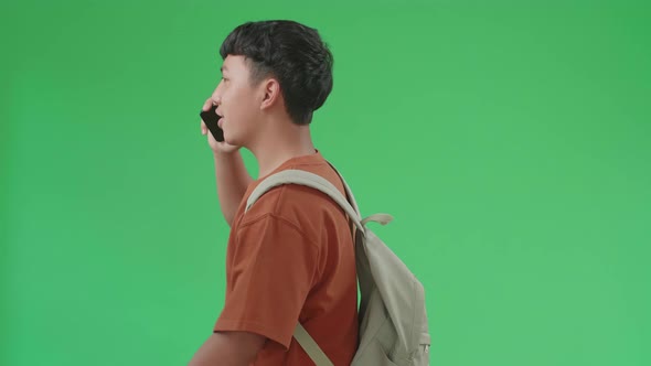 The Side View Of Asian Boy Student Talking On Mobile Phone While Walking To School On Green Screen