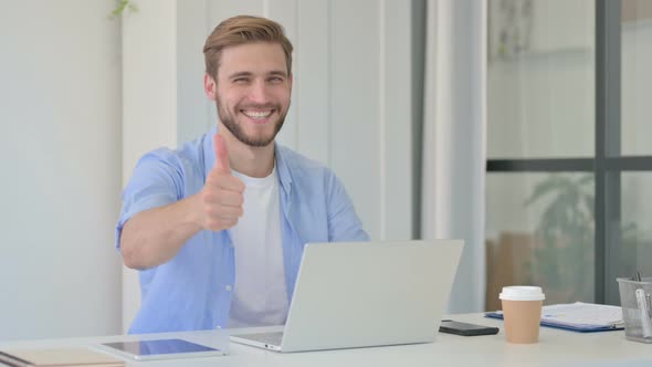 Thumbs Up By Young Creative Man with Laptop at Work
