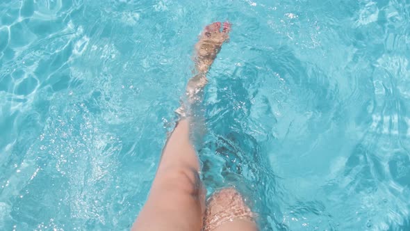 Female sitting on poolside, splashing water with legs, Clear crystal water in Slow motion