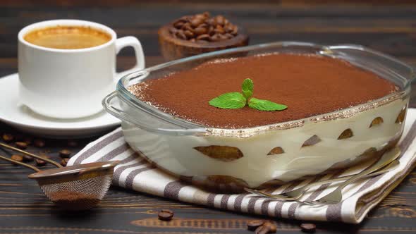 Tiramisu Dessert in Glass Baking Dish and Cup of Fresh Hot Espresso Coffee on Wooden Background