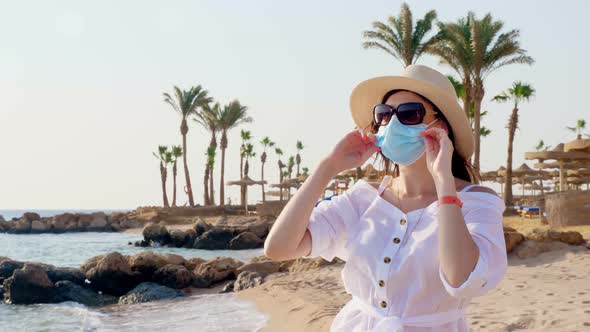 Woman in Protective Mask, Sunglasses and Sun Hat, Takes Off Mask and Breathing Fresh Air, Against