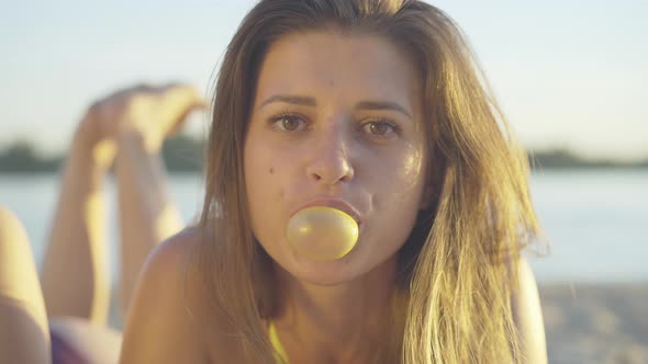 Close-up Face of Young Pretty Brunette Woman with Brown Eyes Blowing Chewing Gum in Sunlight