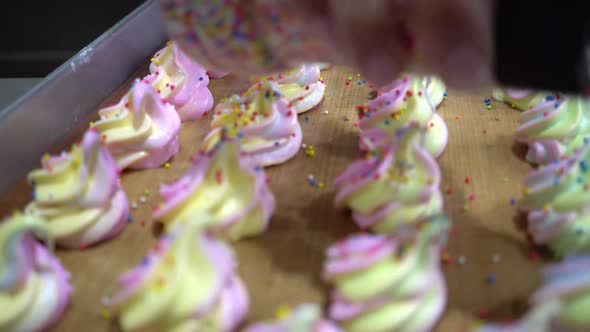 Closeup of Chef Hand Scattering Sugar Sprinkles on Colorful Rainbow Meringues on Tray in Kitchen