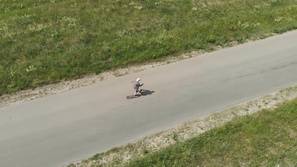 Man Rides at Straight Road on Longboard at Sunset Time Aerial . The Guy Rides a Longboard on the Way